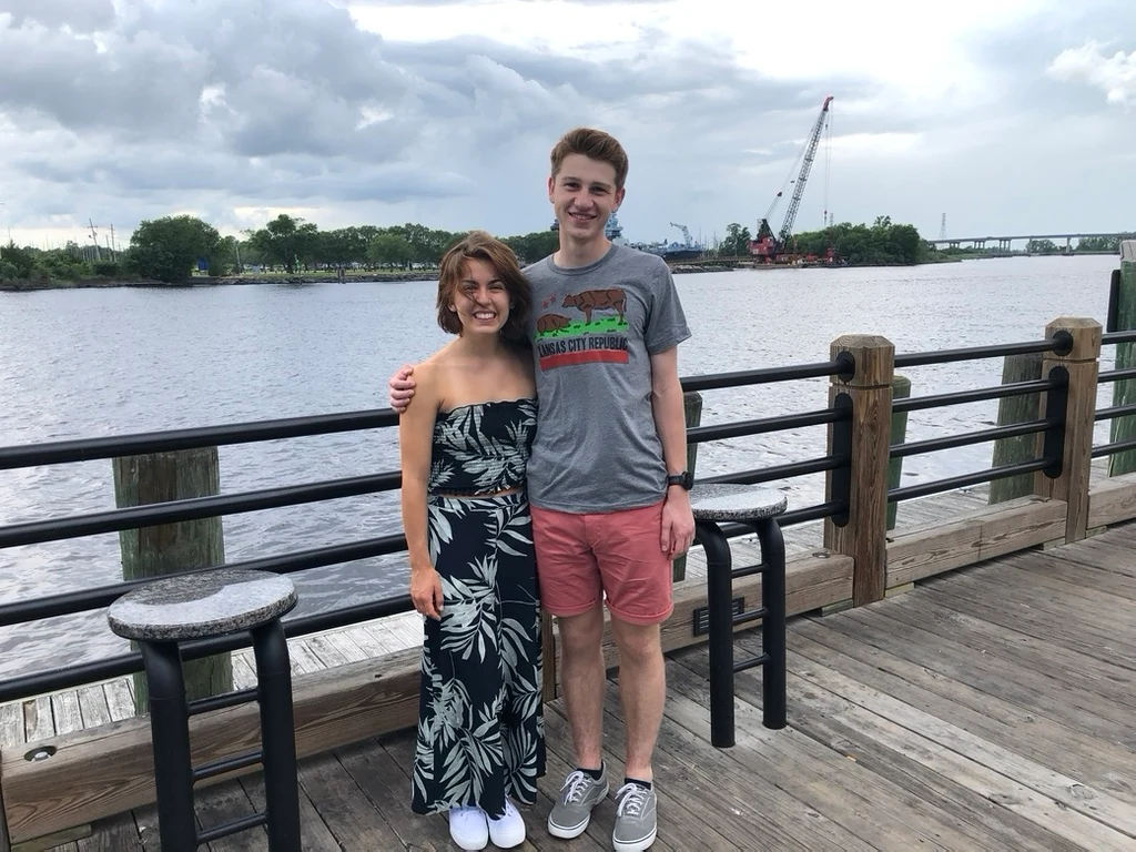 Anna Margaret and Hugh standing together on a waterfront boardwalk
